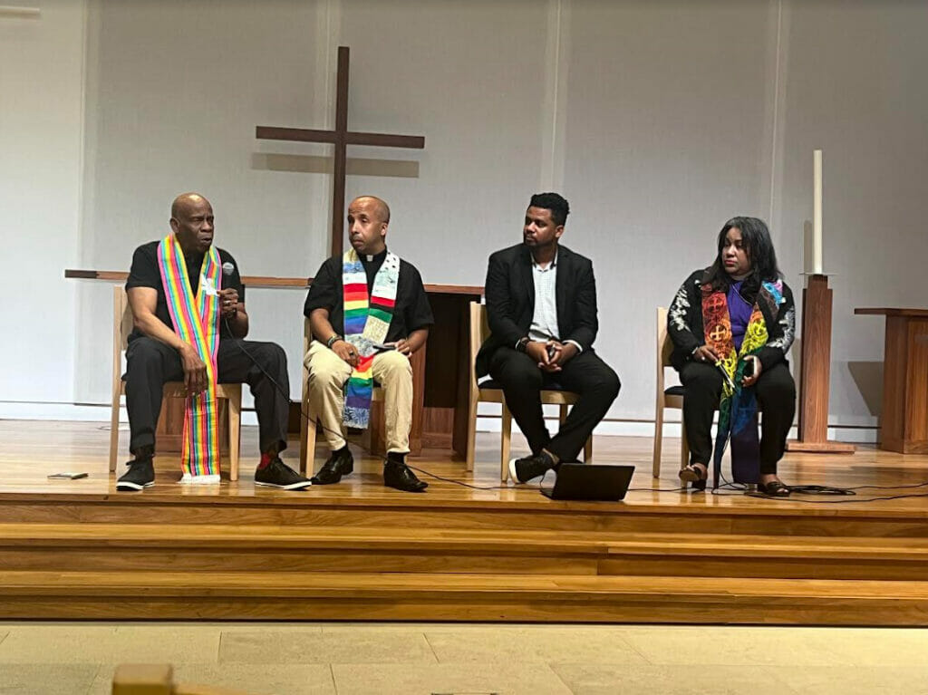 (From left to right) Rev. Dr. Chuck Rhodes, Rev. Jason Carson Wilson, Rev. Redeem Robinson, and Bishop Allyson Abrams in rainbow sashes, in front of a cross on the steps inside the First Congressional UCC Church