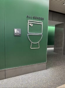 Kansas City Airport | GLAAD Kansas City Airport, green wall with a picture of a toilet in silver metal with "All-Gender" restroom on the green wall above speckled tile floor.