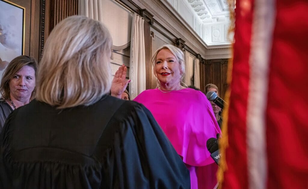 Olivia Hill raises her right hand as she is sworn into office. She's wearing a bright pink dress.