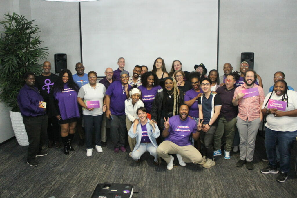About 30 people wearing mostly purple group together, smiling, with their arms wrapped around each other in celebration of completing a four hour media training "Telling Your Story" with the GLAAD Media Institute in Las Vegas September 30, 2023
