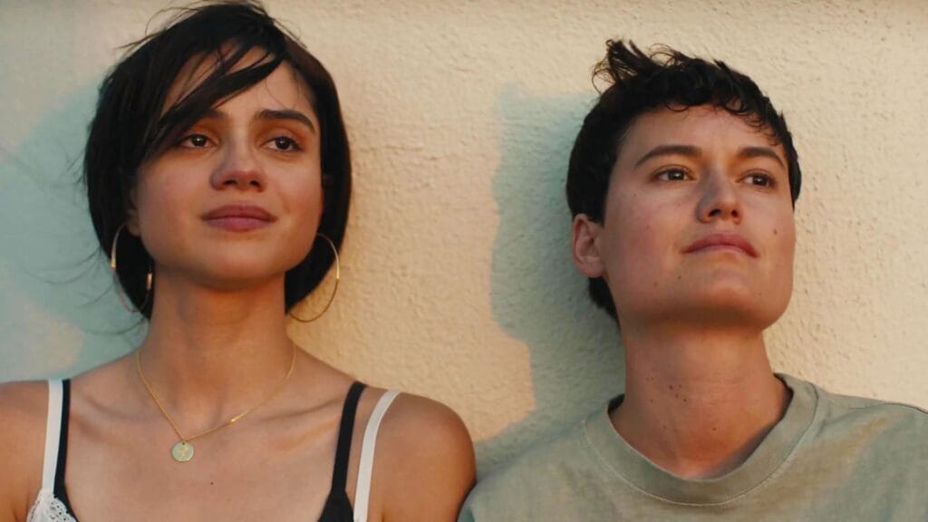Two siblings stand next to each other leaning on a wall in sunset lighting, looking into the distance
