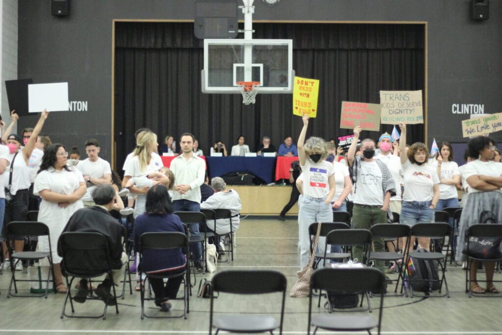 IMG_0053 | GLAAD Activists fill Clinton Middle School to protest Resolution #248, an anti-trans sports ban. People in white shirts with signs that read "rescind the resolution" and more. A basket ball hoop is behind them hanging over the CEC D2 council looking at the backs of activists