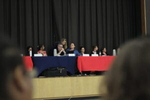 IMG_0091 | GLAAD Maud Maron, blonde long hair, white in a dark suit, whispers to CEC D2 President Len Silverman, white, dark brown hair.