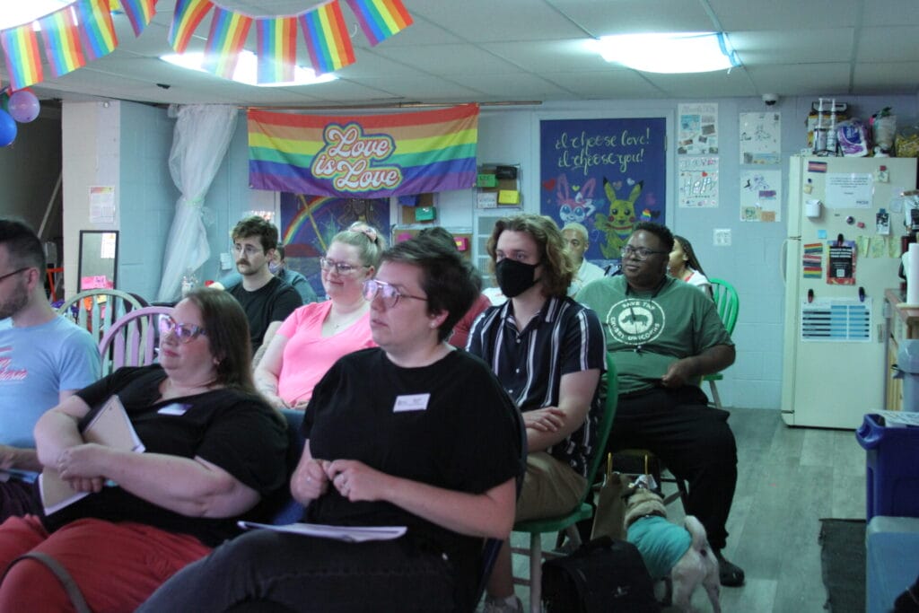 Members from the LGBTQ community of Grand Rapids, MI meets with GLAAD. Pride flags and streamers hang throughout the room for which people sit.