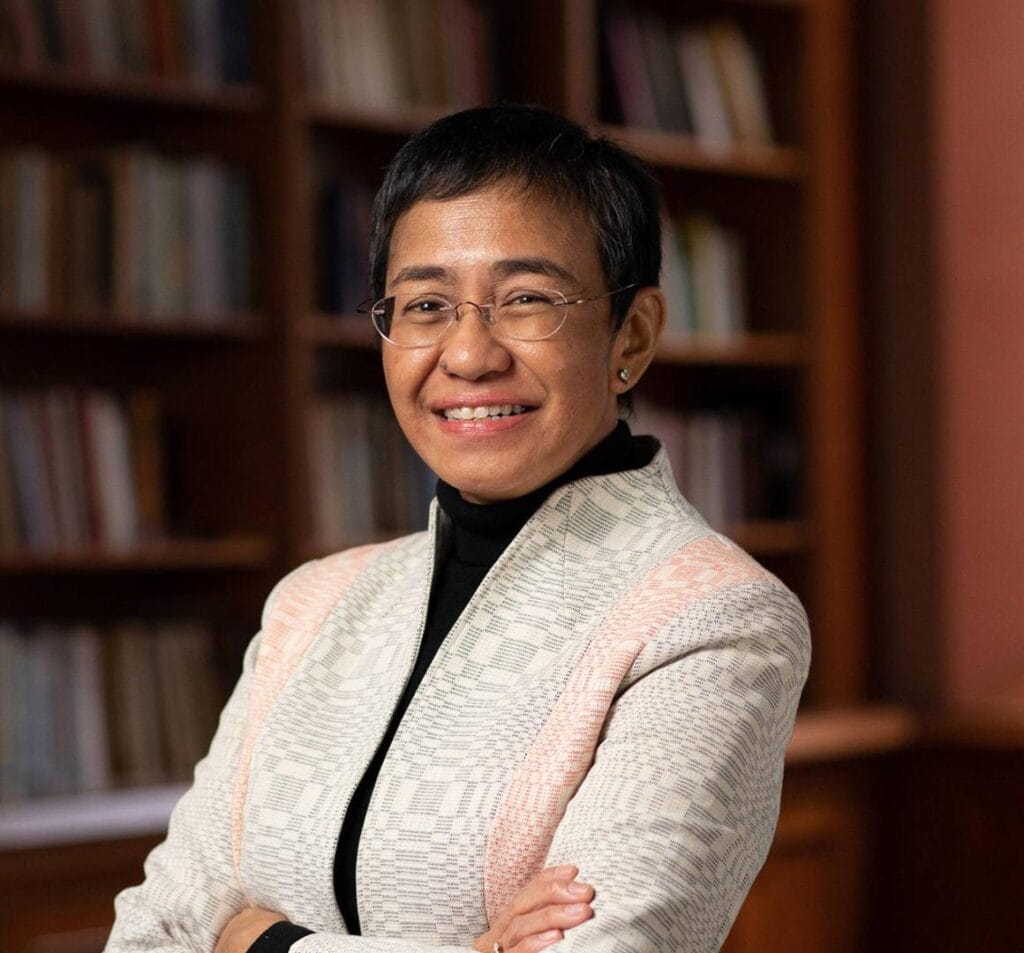 Maria Ressa Princeton | GLAAD a short brown-skinned Filipina woman with a neat pixie cut hairstyle, oblong glasses, a black turtleneck, and fuschia blazer