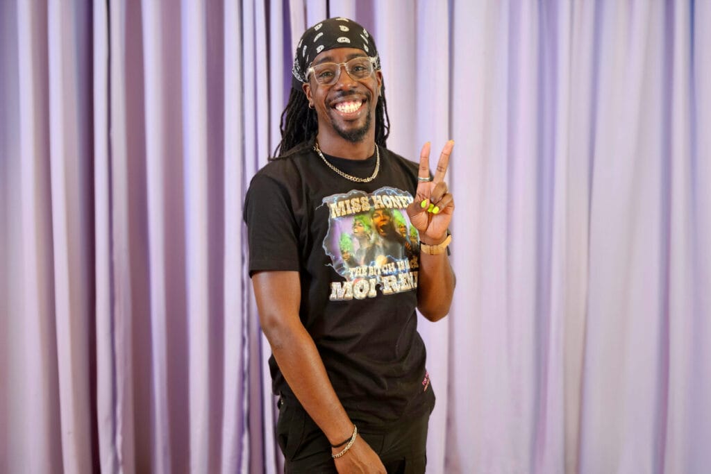 Creative and Filmmaker Brandon Nicholas stands wearing a black shirt, black bandana, and black pants posing in front of a purple backdrop.