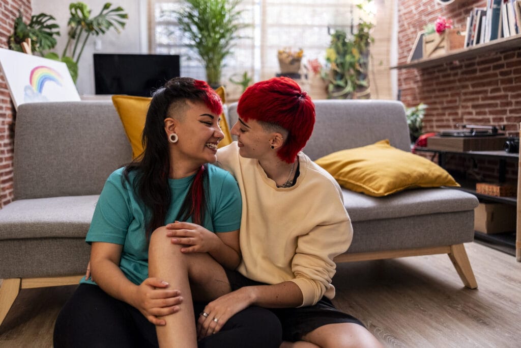 two young lesbian women at home on the floor next to the sofa in love | GLAAD
