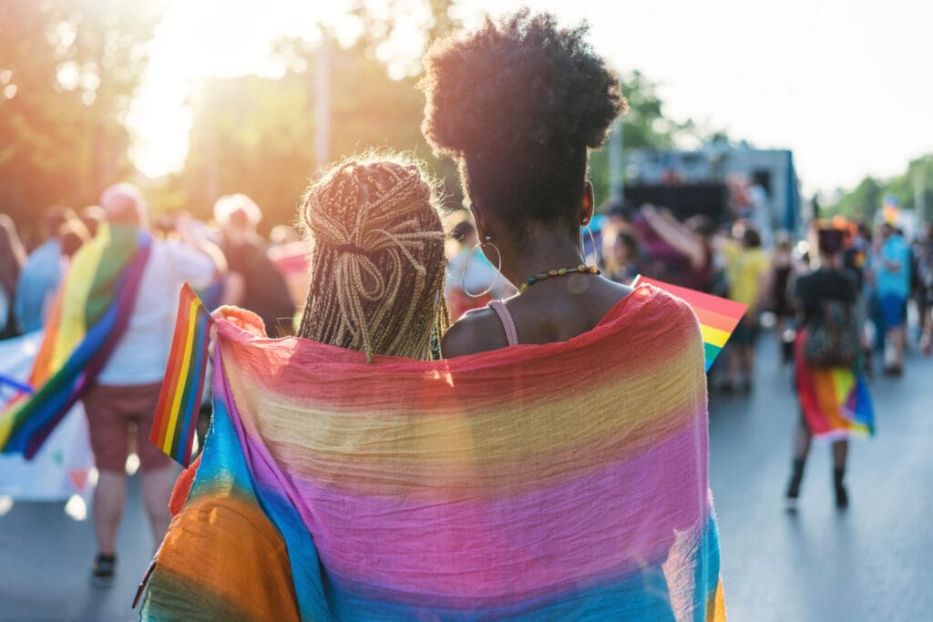Young female couple hugging with rainbow scarf at the pride event | GLAAD