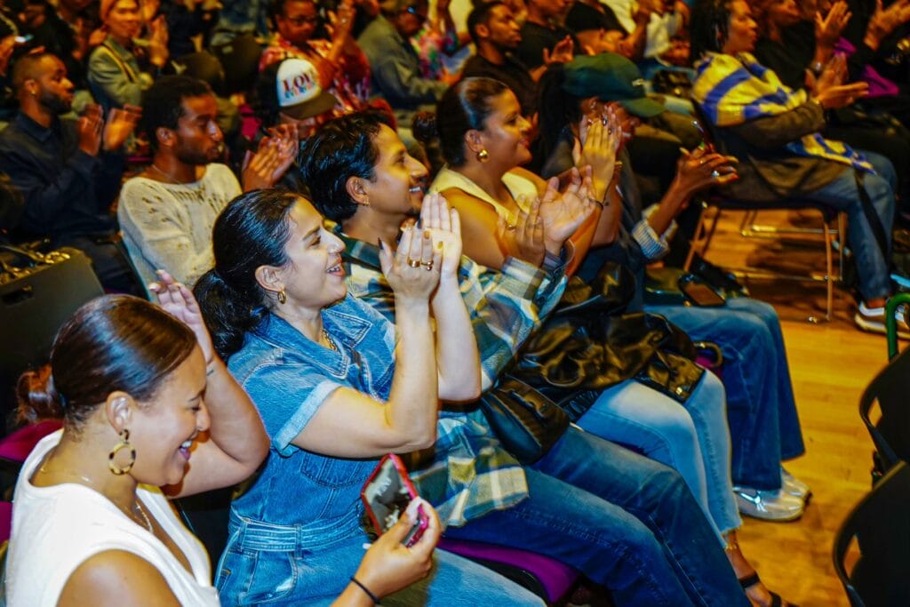 image_50802177 | GLAAD Audience claps as film ends, the photo shows a diagonal image of rows of bodies smiling and clapping in a low-light room