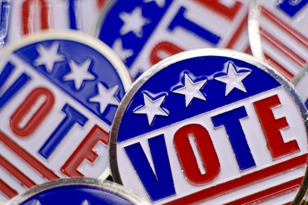 Full frame shot of pins that say “vote” with red, white, and blue American flag theme. No people.