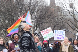 IMG_2634 | GLAAD Kristin Clifford speaks to crowd about her and her families experiences with leading healthcare facilities in NYC. The progressive pride flag and signs swirl around her as she speaks into the air.