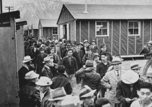 GettyImages-1388588888 | GLAAD Japanese Americans detainees walk among the accommodation cabins of the Manzanar War Relocation Center in Owens Valley, Inyo County, California, 23rd March 1942. Approximately 11,000 Japanese Americans were detained at Manzanar, one of ten American internment camps during World War II. (Photo by UPI/Bettmann Archive/Getty Images)