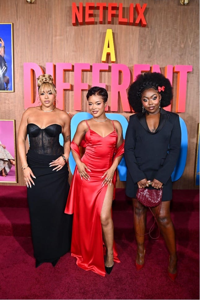 Three women pose on the red carpet at a Netflix premiere, wearing evening gowns.