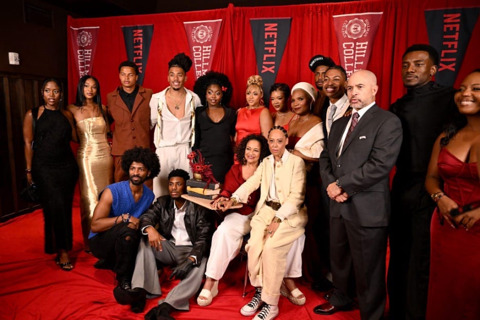 Diverse group posing on a red carpet with Netflix banners in the background, centered around a trophy they’re presenting.