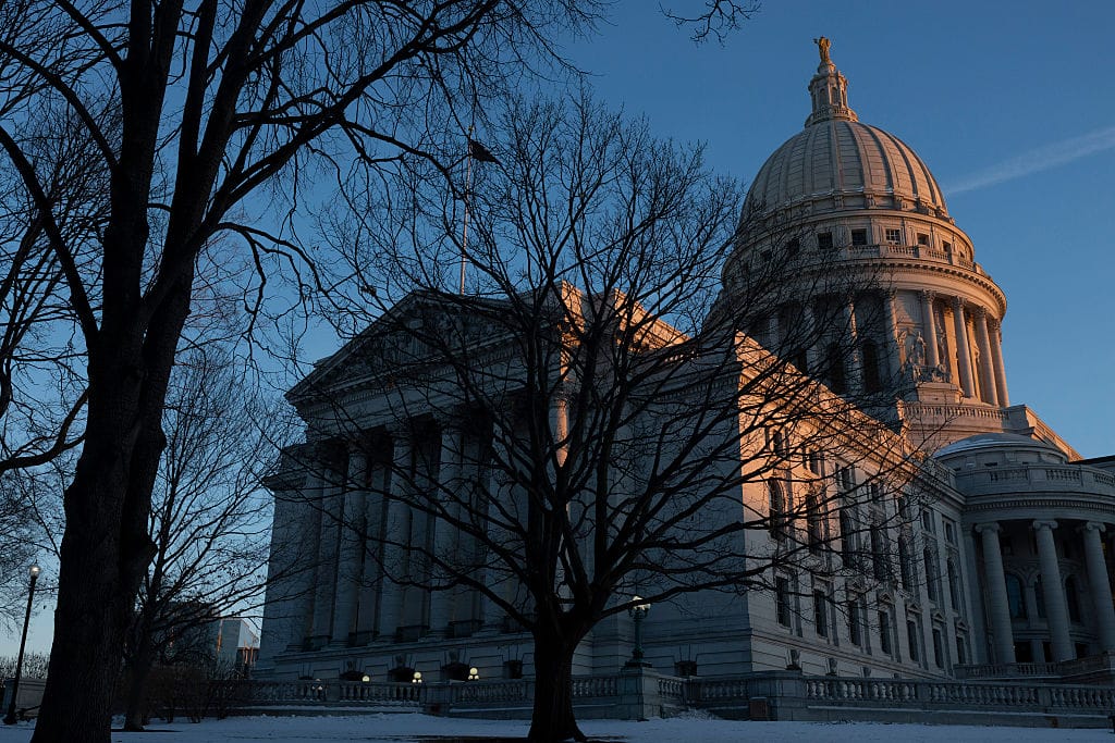 Wisconsin State Capitol | GLAAD Capitol building with a domed roof and neoclassical columns, seen through bare trees at dusk with snowy ground.