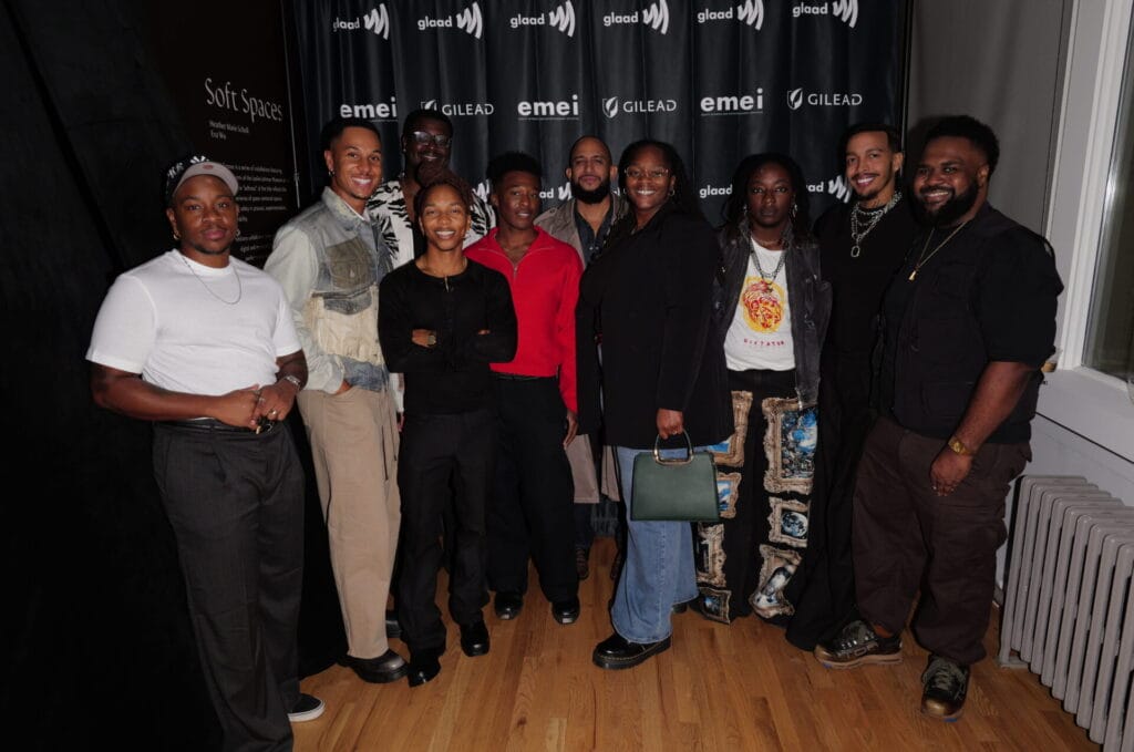 Group of diverse adults posing together in a backstage area, smiling, in front of a black backdrop with glaad and emei logos.