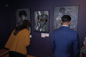 Two visitors observe black-and-white astronaut portraits on a purple gallery wall.